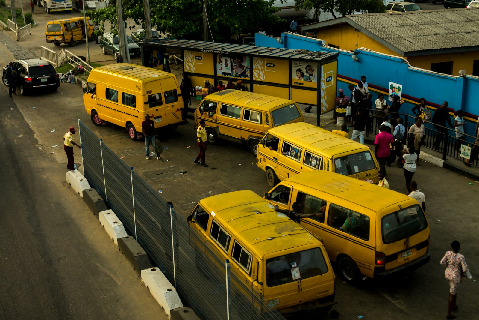 Yellow danfo buses parked at a Lagos bus stop with people waiting beside them