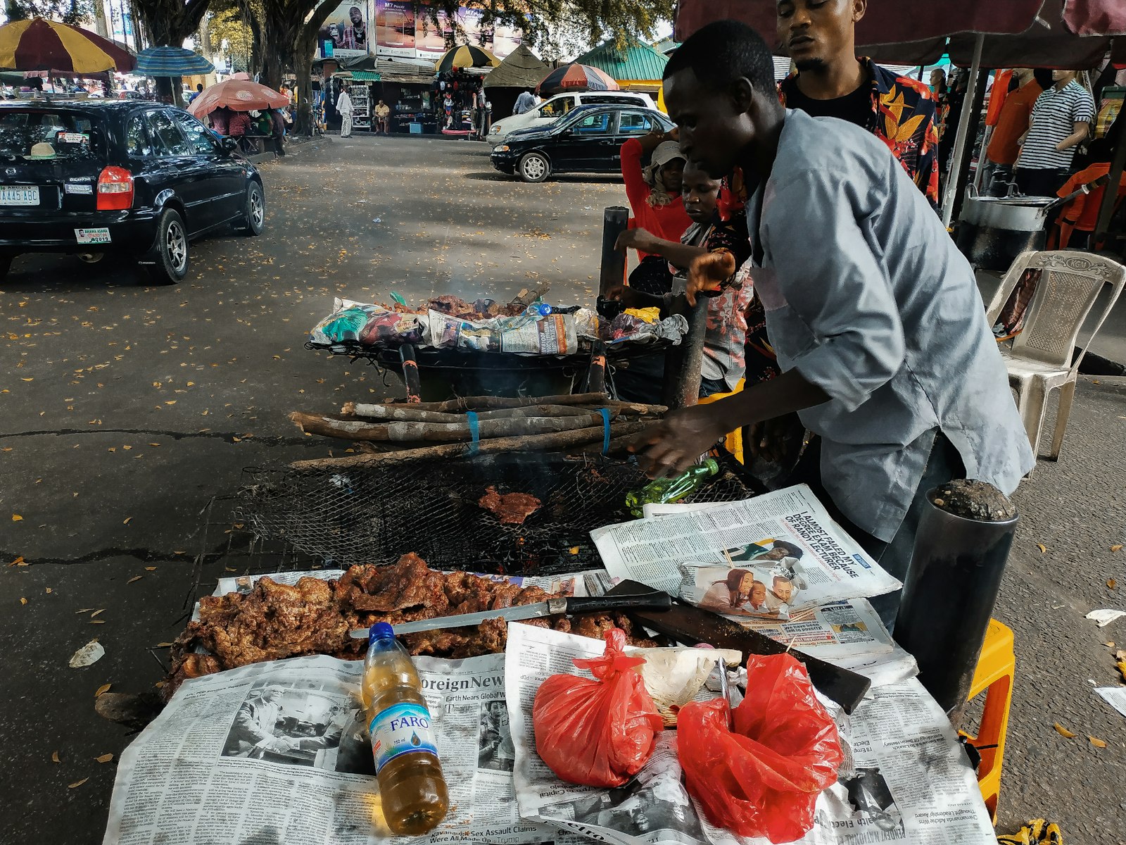 A roadside suya grill in Nigeria, with grilled meat laid out on newspaper and a man turning the meat over the coals